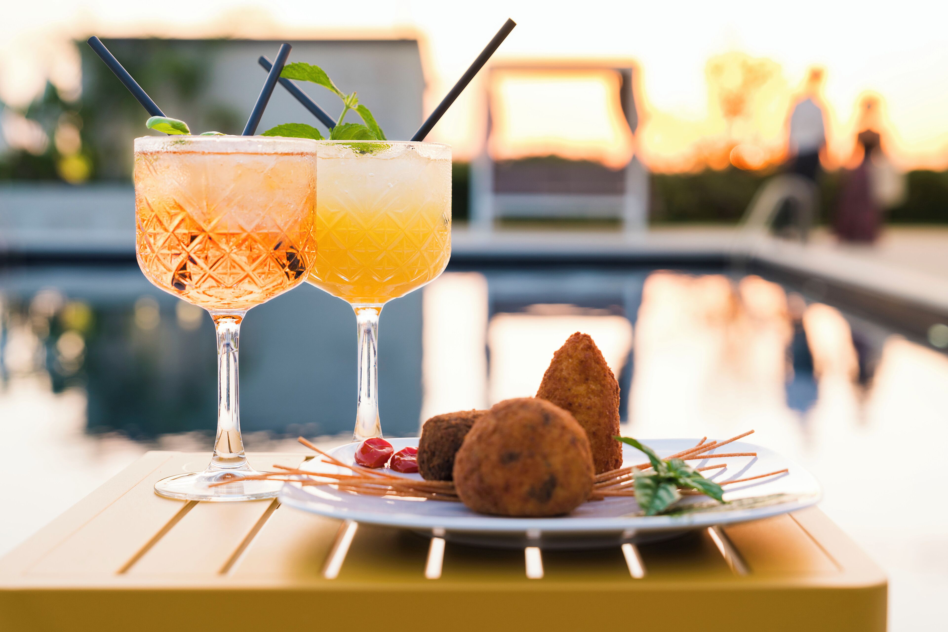 Two cocktails on a table with a pool in the background.