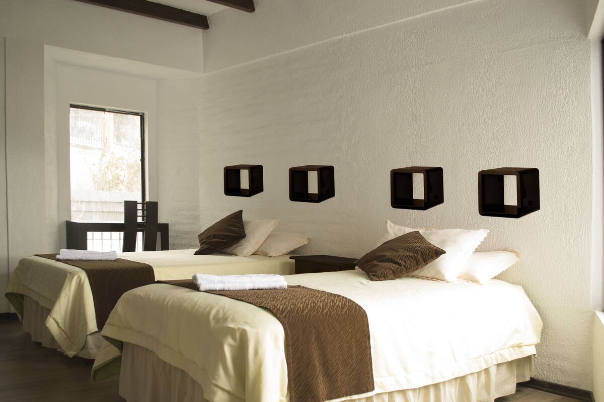 A hotel room with two beds, a window, and wall-mounted shelves.