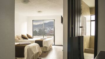 A hotel room with two beds, a large window with a city view, and a flat-screen TV mounted on the wall.