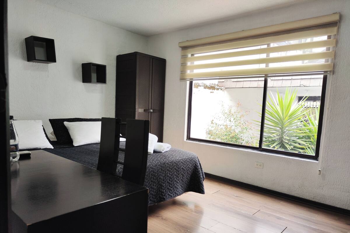 A bedroom with a bed, a desk, and a window with blinds.