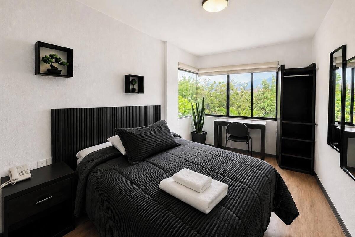 A modern bedroom with a bed, bedside table, and a desk with a chair.