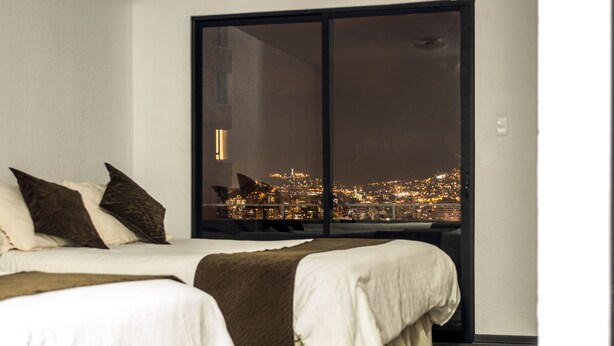Un dormitorio con un ventanal grande que da a una vista nocturna de la ciudad.