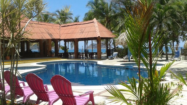 A pool area with a covered pavilion, lounge chairs, and palm trees. - Hotel Brisas del Pacifico (Sámara)
