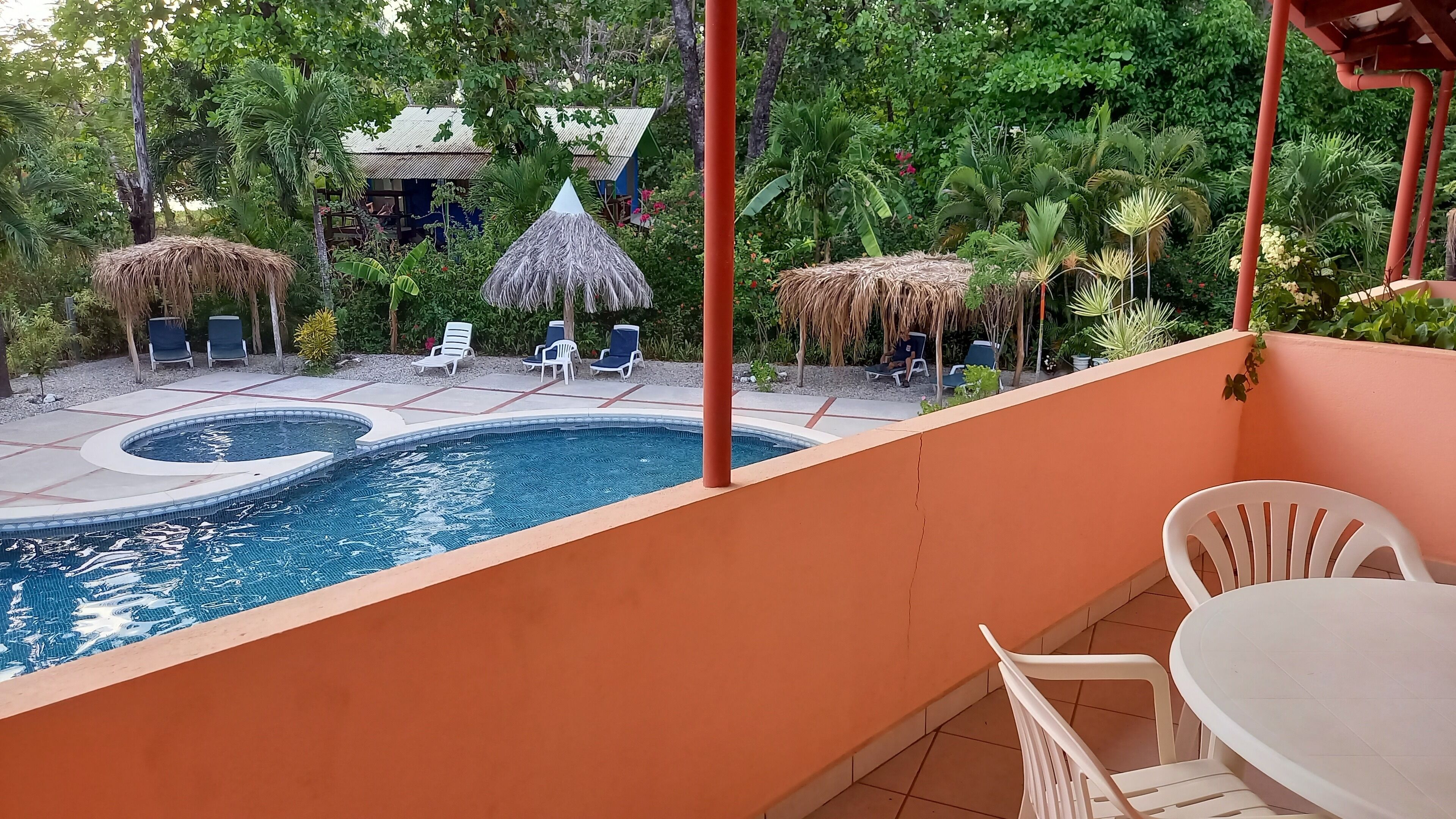 Zona de piscina con dos jacuzzis, sillas de descanso y una sombrilla de paja.