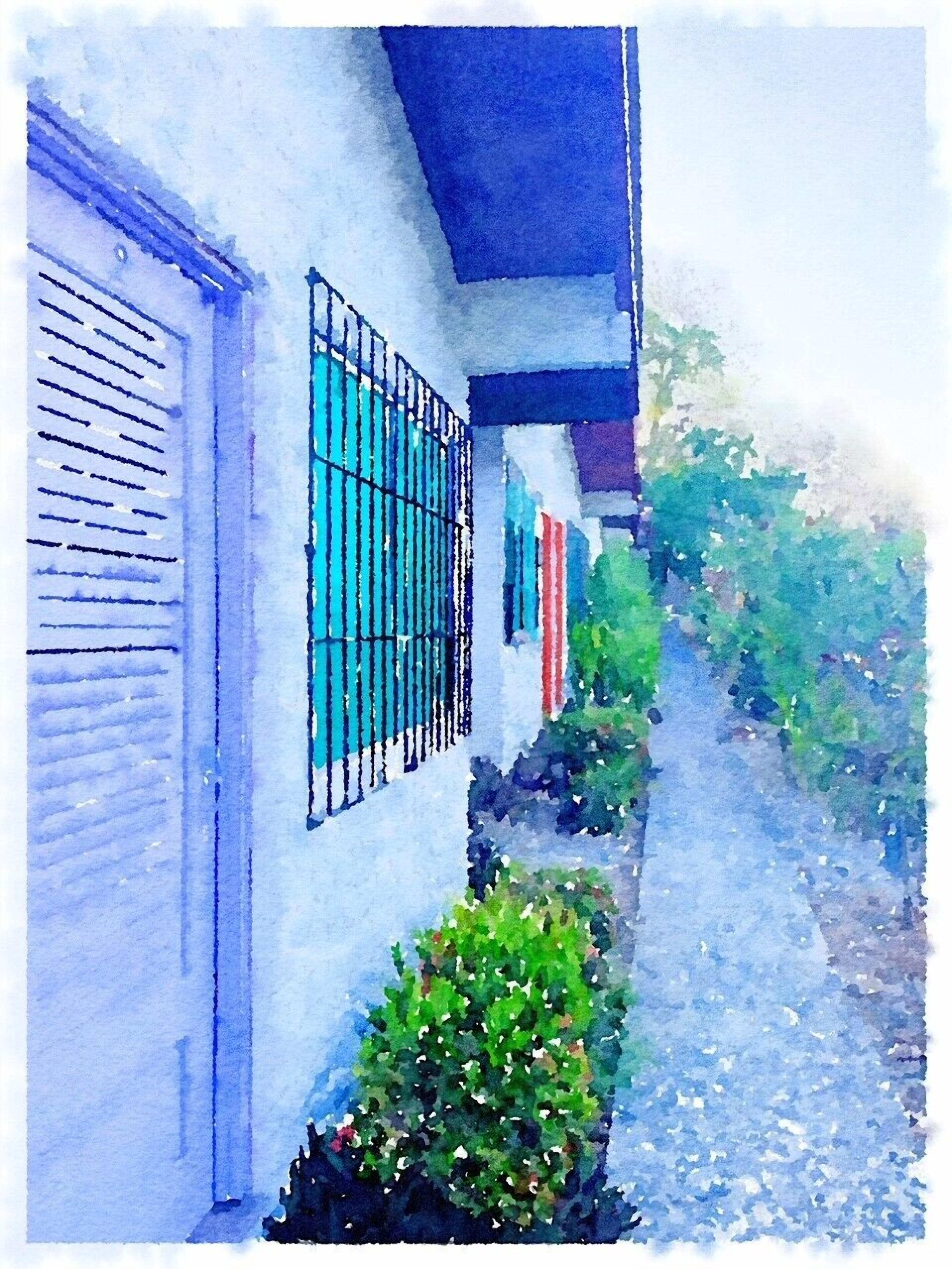 A narrow street with a building featuring a white facade, a blue awning, and a window with a metal grill.