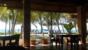 An outdoor seating area with tables and chairs, surrounded by palm trees and a view of the ocean. - Hotel Brisas del Pacifico (Sámara)