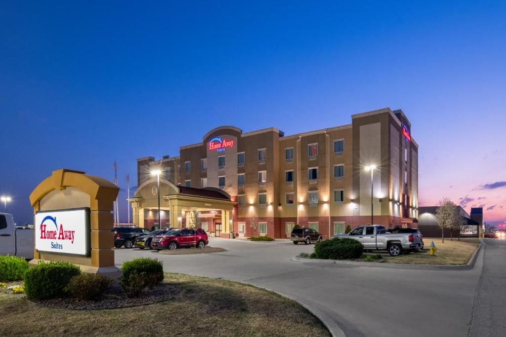 A hotel with a sign reading 'Home Away Suites,' multiple parking spaces, and a well-lit entrance.