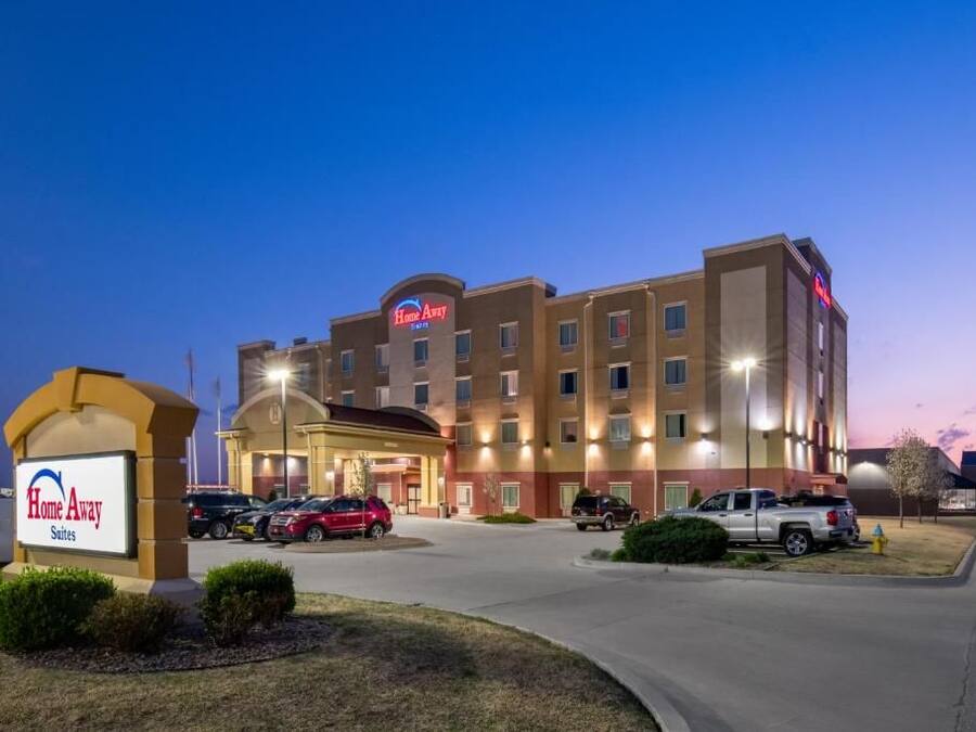 A hotel with a sign reading 'Home Away Suites,' multiple parking spaces, and a well-lit entrance.