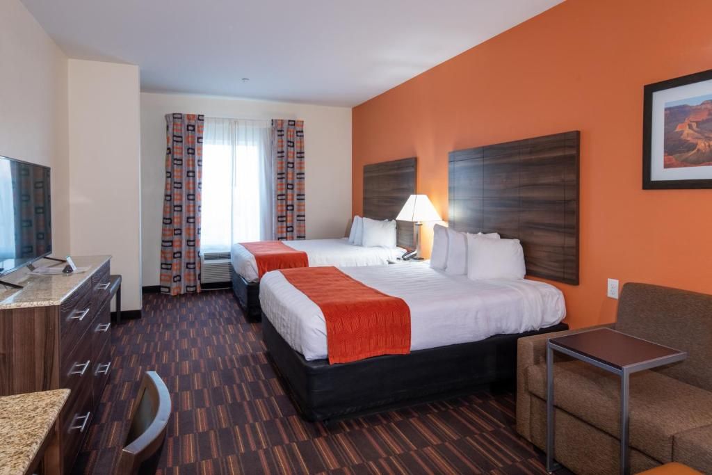 A hotel room with two beds, a desk, a chair, and a television.