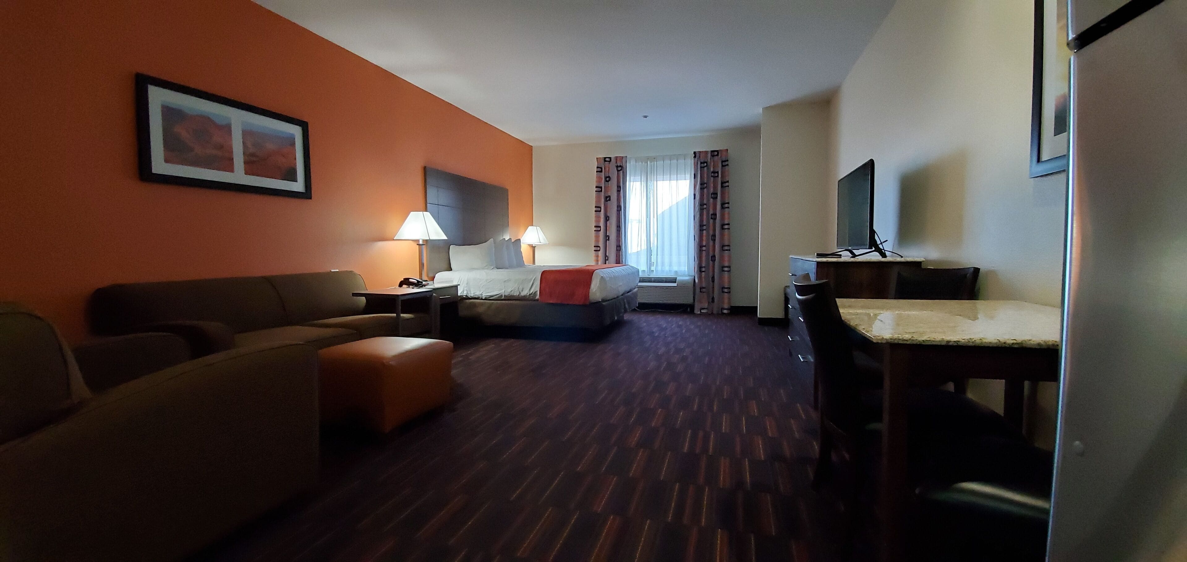 A hotel room with a sofa, a bed, a desk, and a TV.