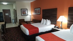 A hotel room with two beds, a desk, chairs, a lamp, and a wall-mounted phone.