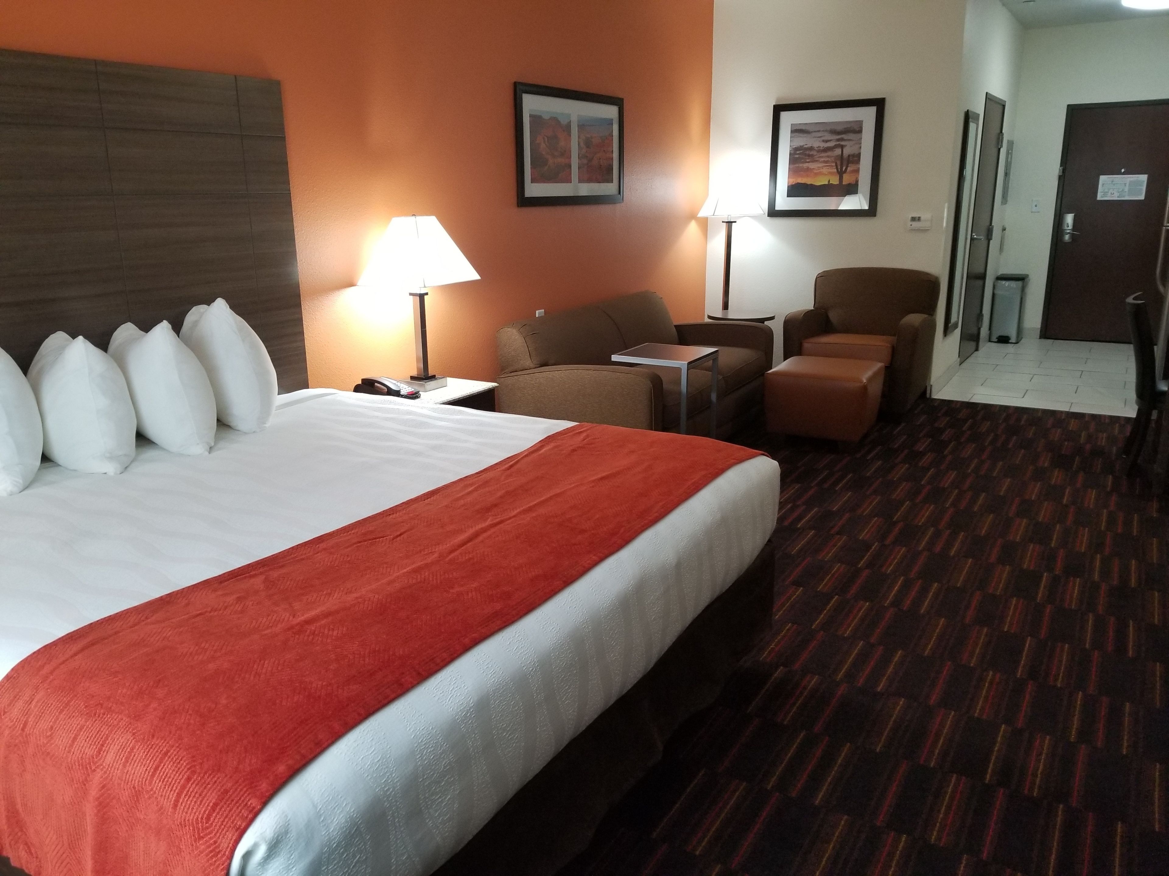 Habitación de hotel con una cama grande, dos sillones, una mesita y un escritorio. Hay dos lámparas sobre la mesa y sillas.
