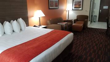 Habitación de hotel con una cama grande, dos sillones, una mesita y un escritorio. Hay dos lámparas sobre la mesa y sillas.
