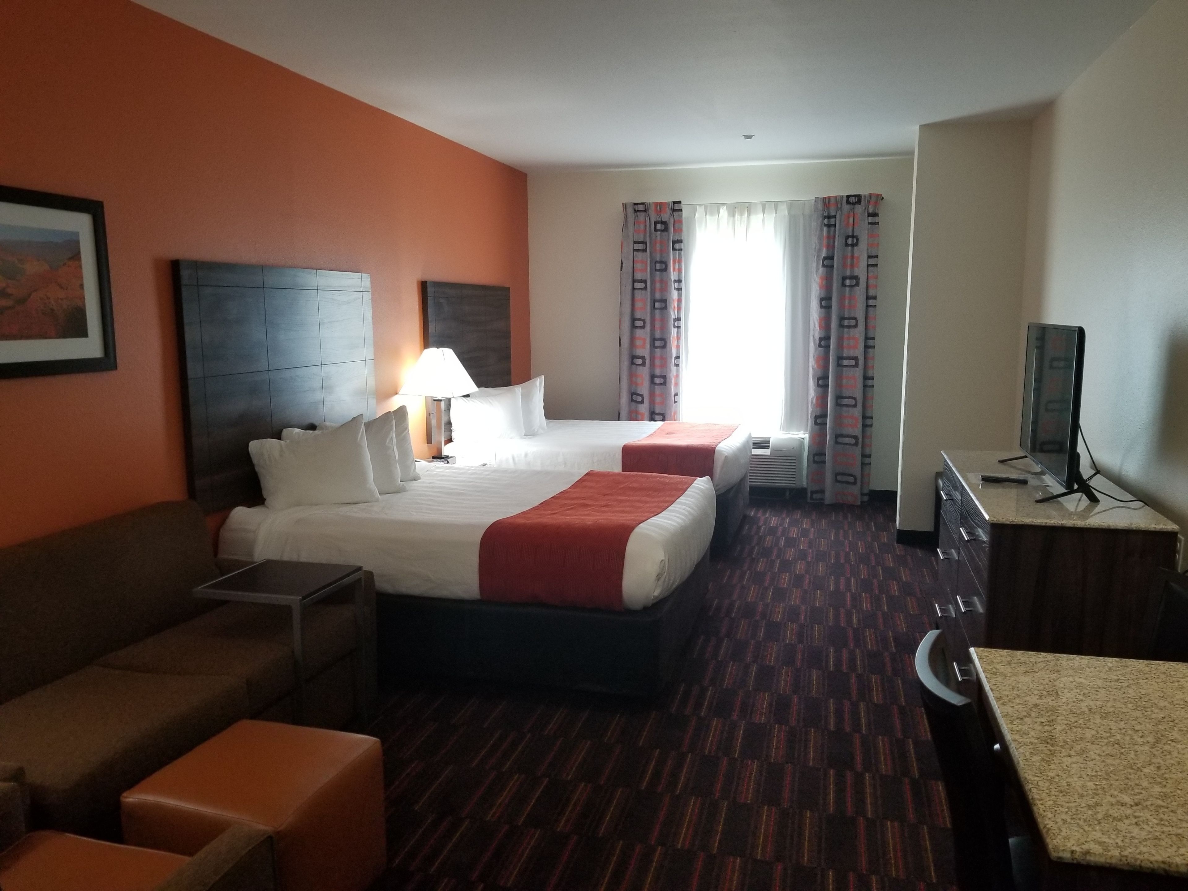 A hotel room with two beds, a desk, a TV, and a sofa.