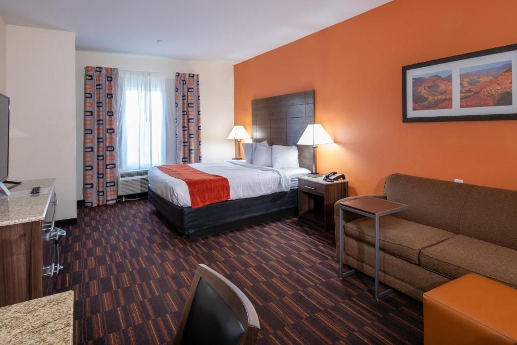 A hotel room with a bed, bedside lamps, a desk, a chair, a sofa, and a framed picture on the wall.