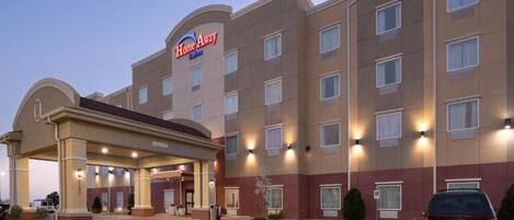 A hotel with a central entrance, multiple floors, and a parking lot.