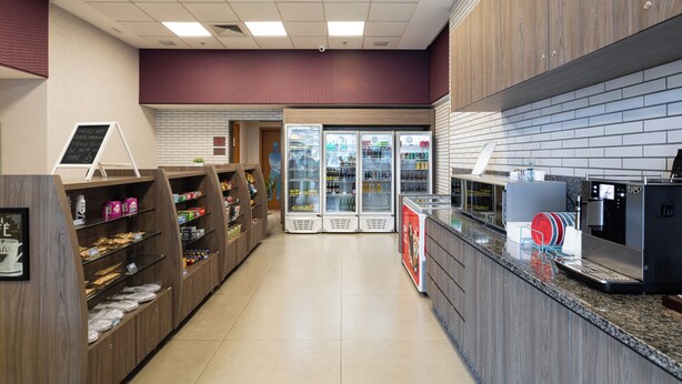 Interior de una cafetería moderna y luminosa, con una máquina de café, vitrinas refrigeradas y un mostrador con un atril para el menú.