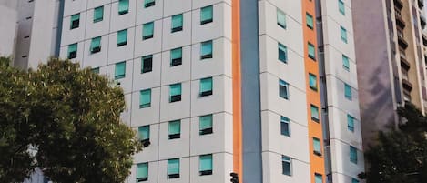Un hotel de varios pisos con diseño moderno, que destaca por su fachada naranja y blanca, múltiples ventanas y una entrada visible con un letrero.