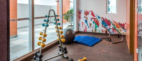 Un gimnasio con equipo de ejercicio, una pelota grande y un mural colorido en la pared.