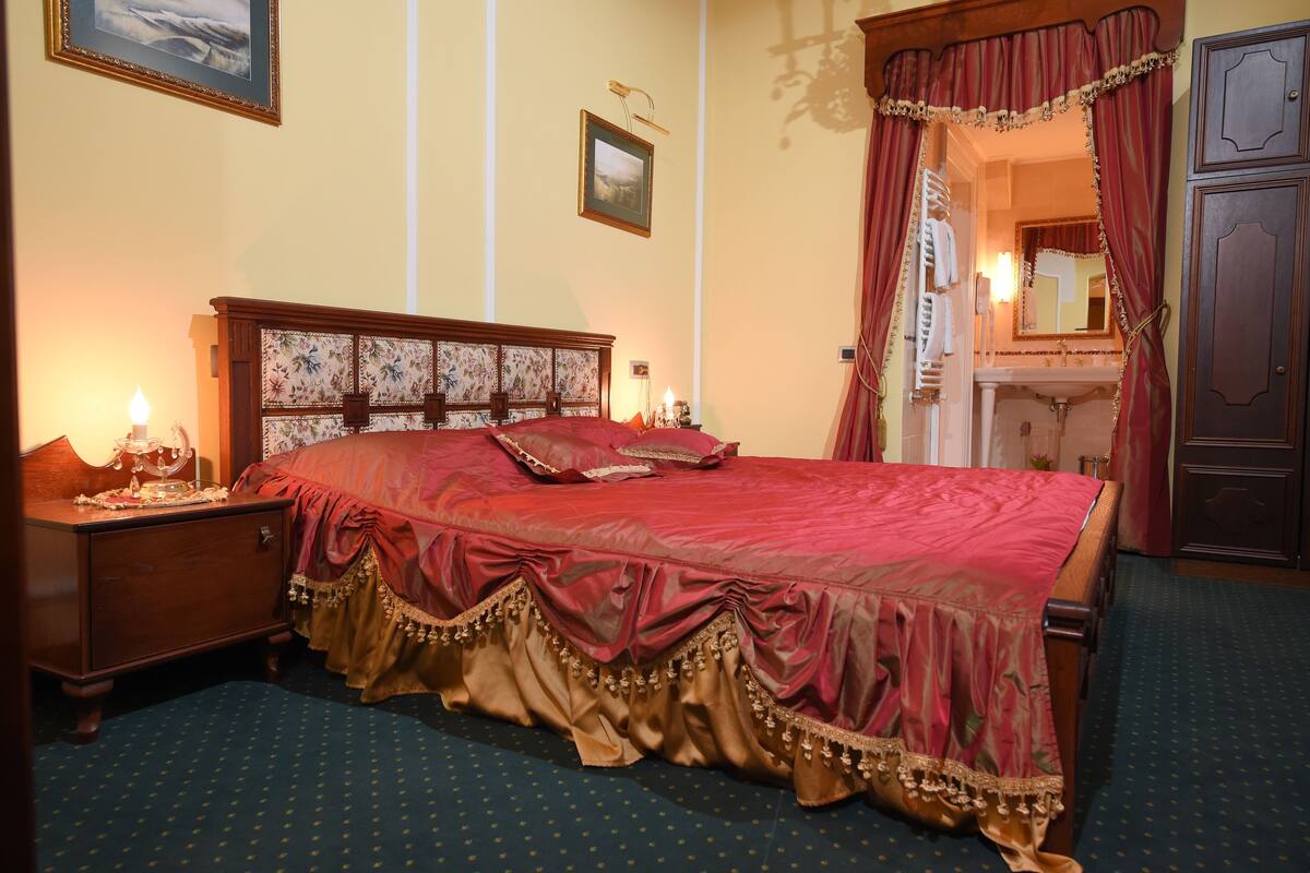 A traditional bedroom with a large bed, a nightstand, a mirror, and a wardrobe.