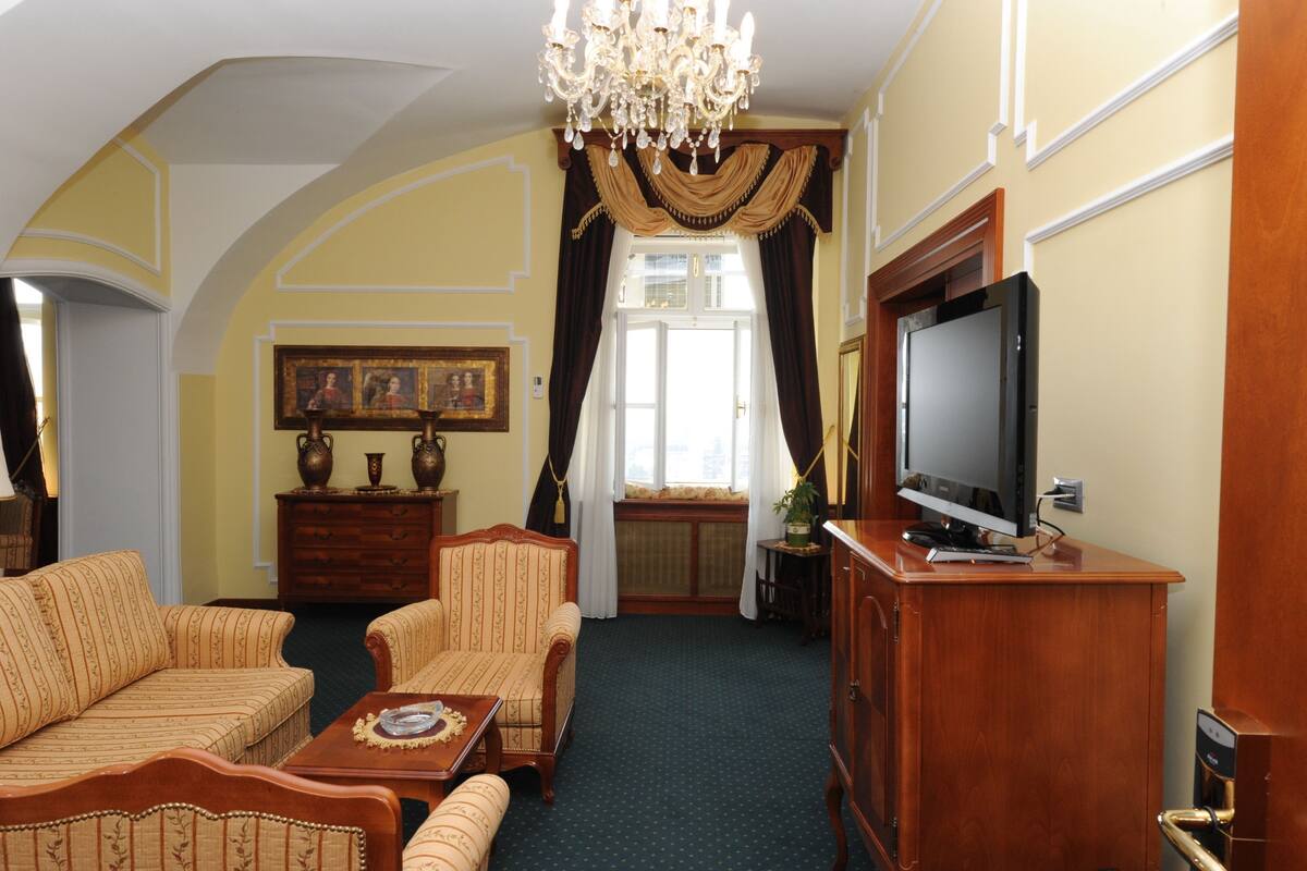 A room with a chandelier, a television on a wooden cabinet, a sofa, a chair, and a cabinet with decorative items.