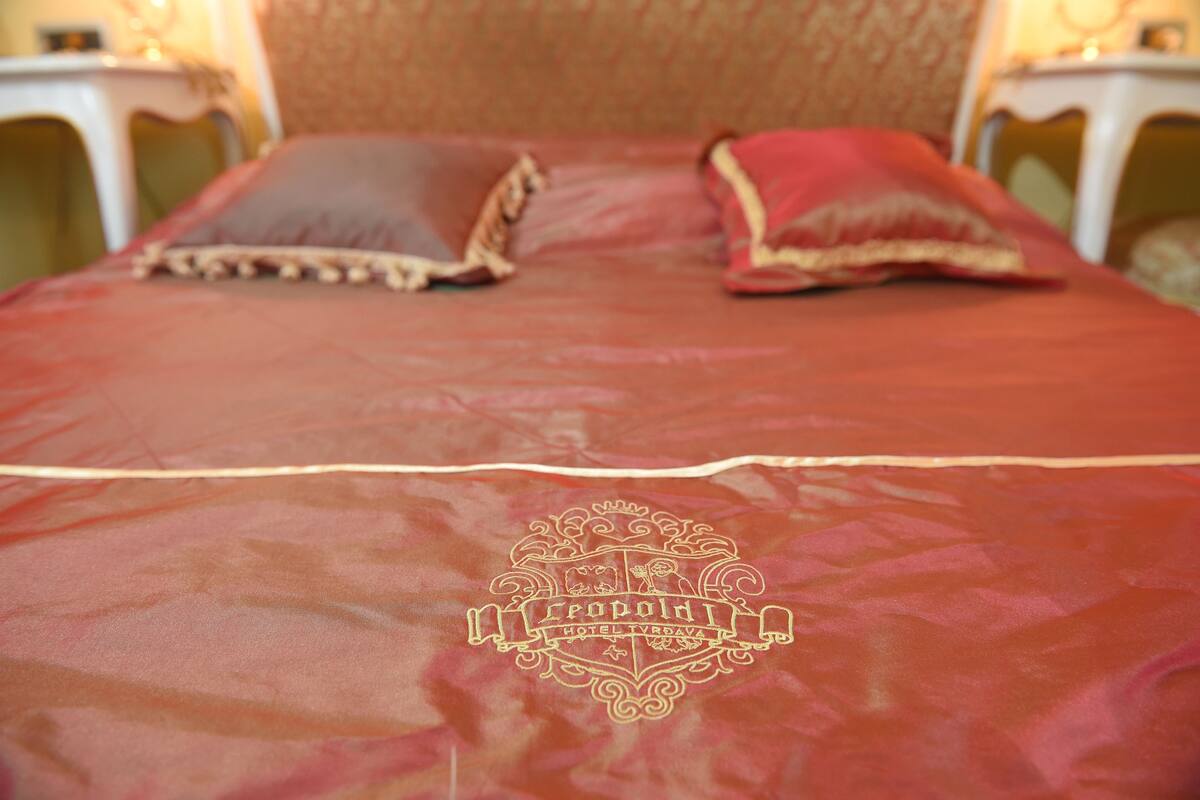 A bed with a red bedspread and a crest emblem.