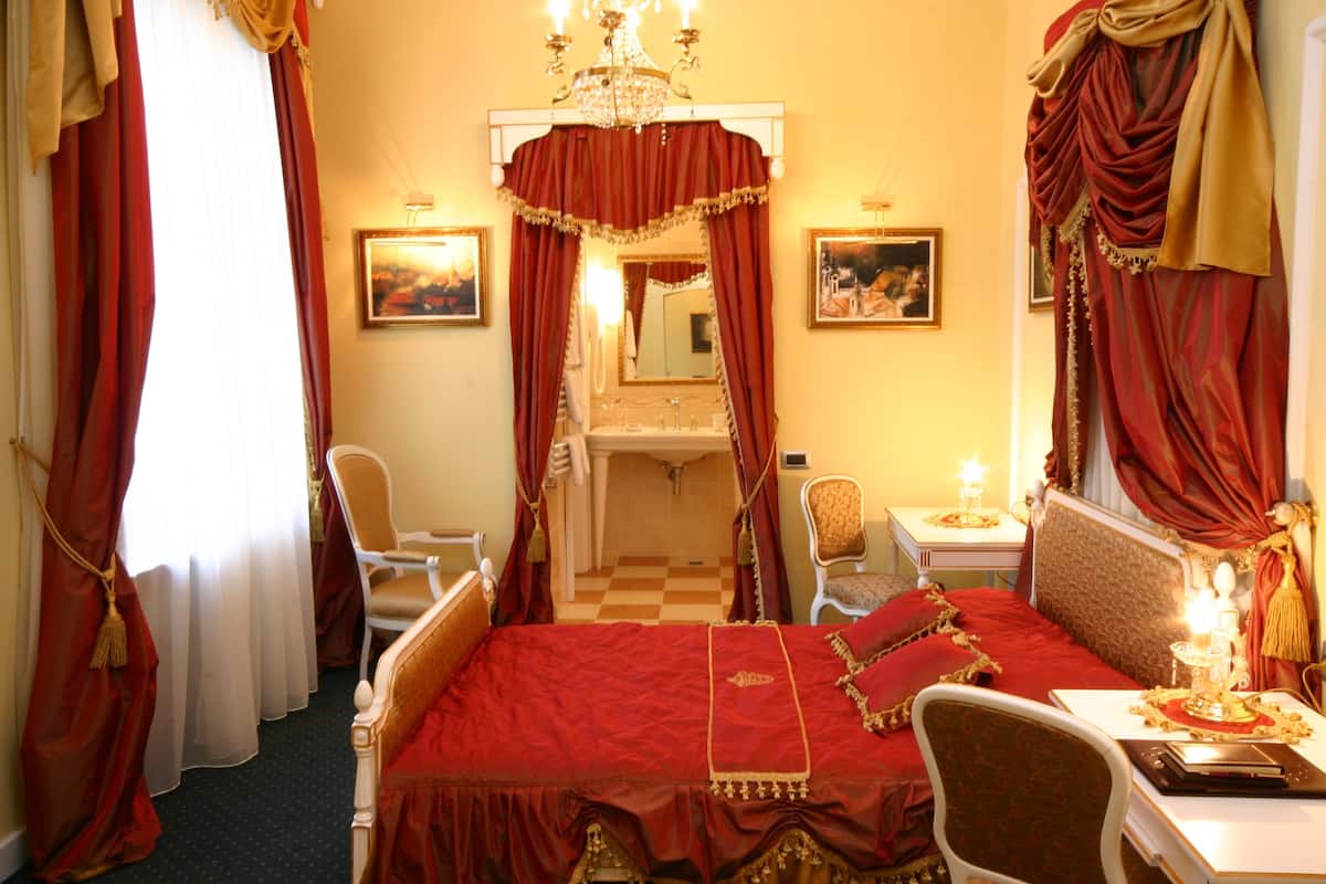 A room with a large bed, a chair, a vanity with a mirror, and a chandelier.