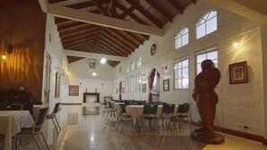 A spacious hall with high ceilings and large windows, featuring a central stage and multiple tables and chairs arranged for events. - Hotel Ave del Paraíso (Mercedes)