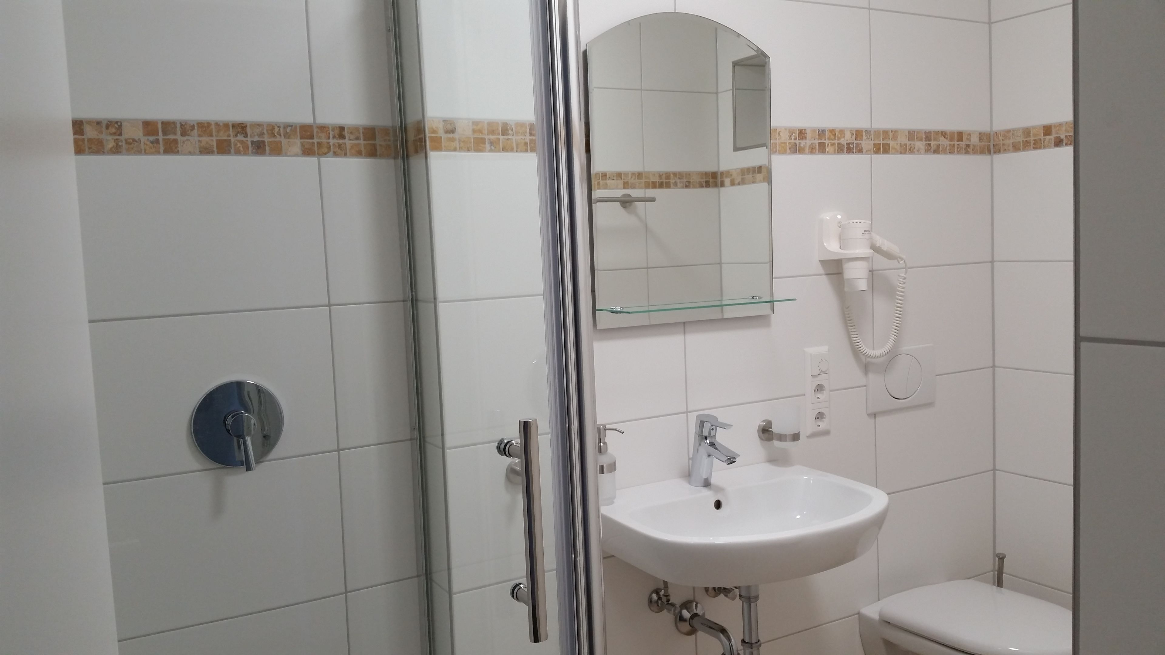 Un baño con cabina de ducha de vidrio, un lavabo blanco, un espejo y un inodoro.
