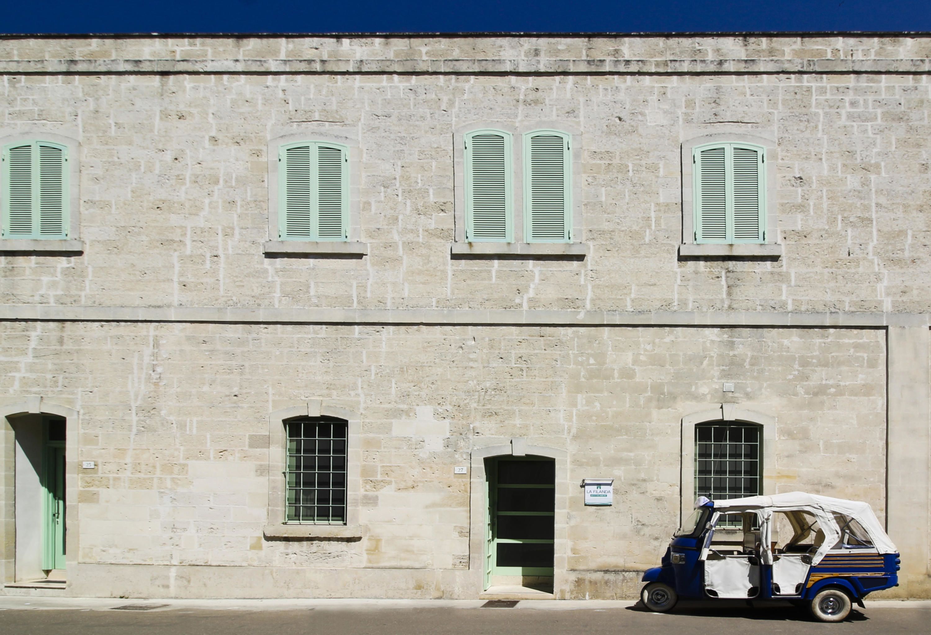 A stone building with multiple windows and a tuk-tuk parked in front.