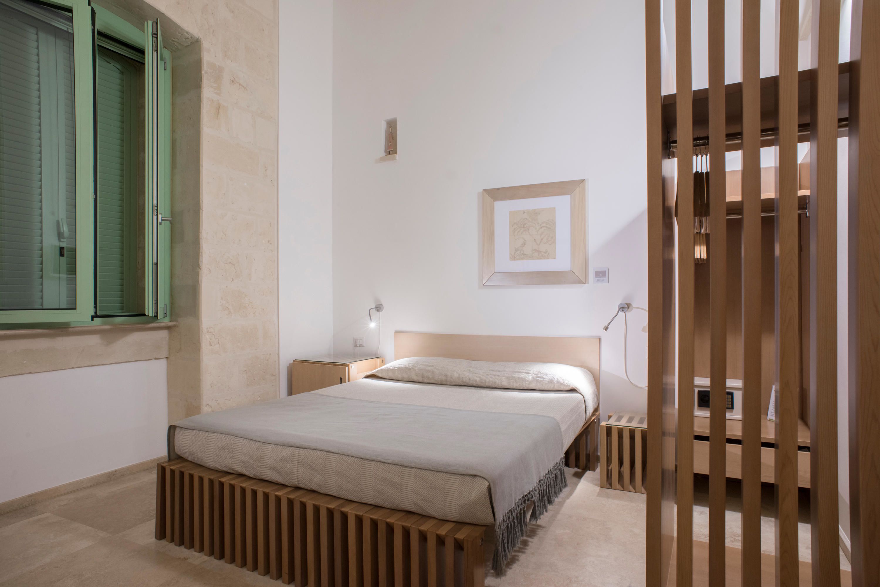 A bedroom with a bed, bedside tables, a nightstand, a wall-mounted light, and a framed picture.