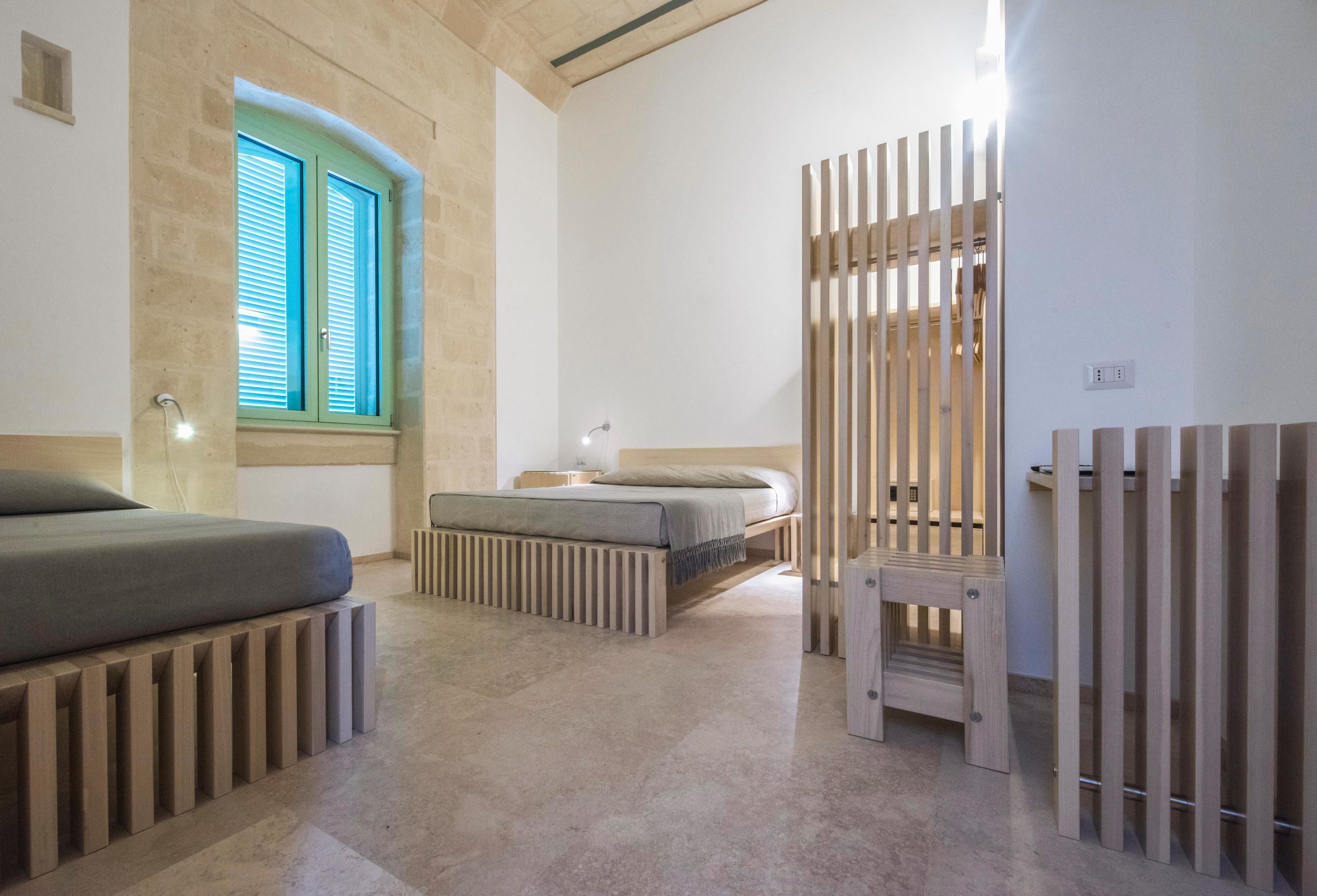 A modern bedroom with a bed, a window with shutters, a bedside table, and a wooden partition.