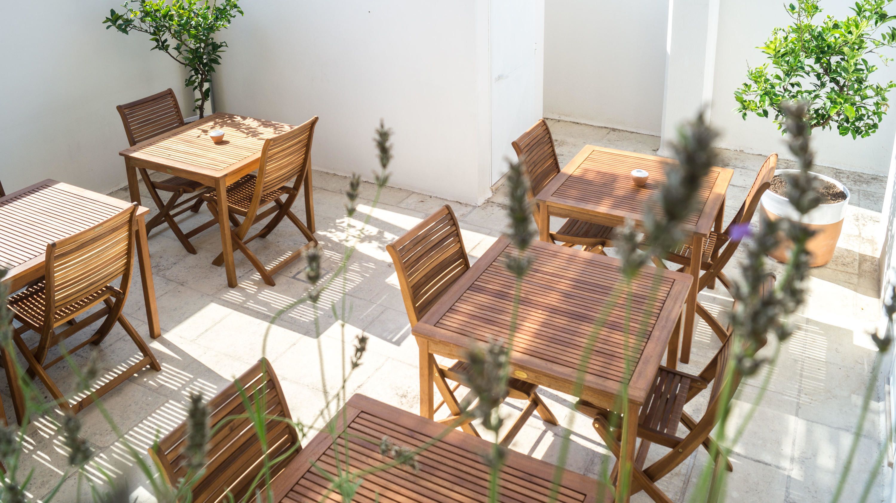 An outdoor patio with wooden tables and chairs, surrounded by potted plants and a clear view of the sky.