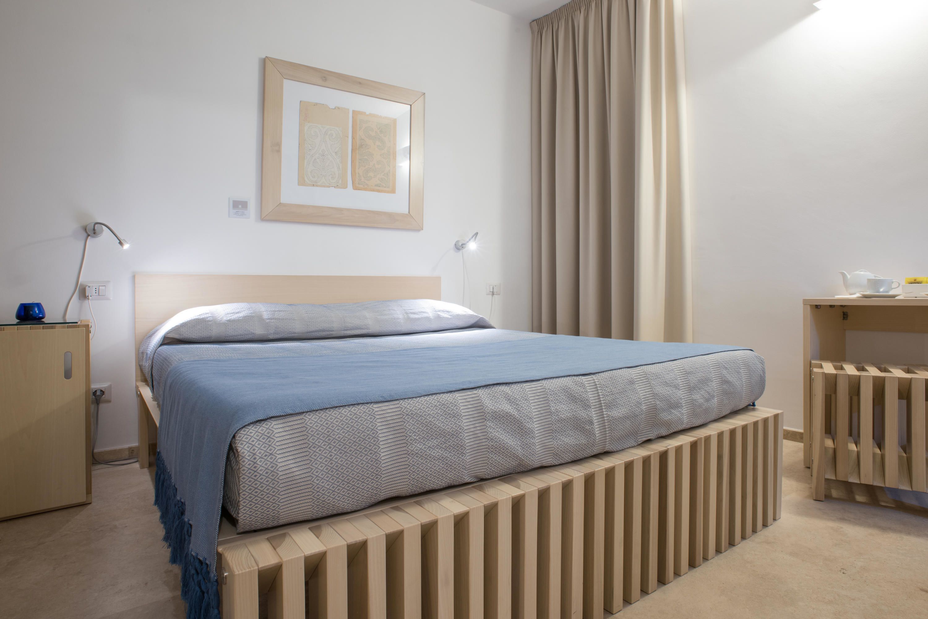Un dormitorio ordenado con cama, lámparas de noche, mesita de noche y un cuadro en la pared.
