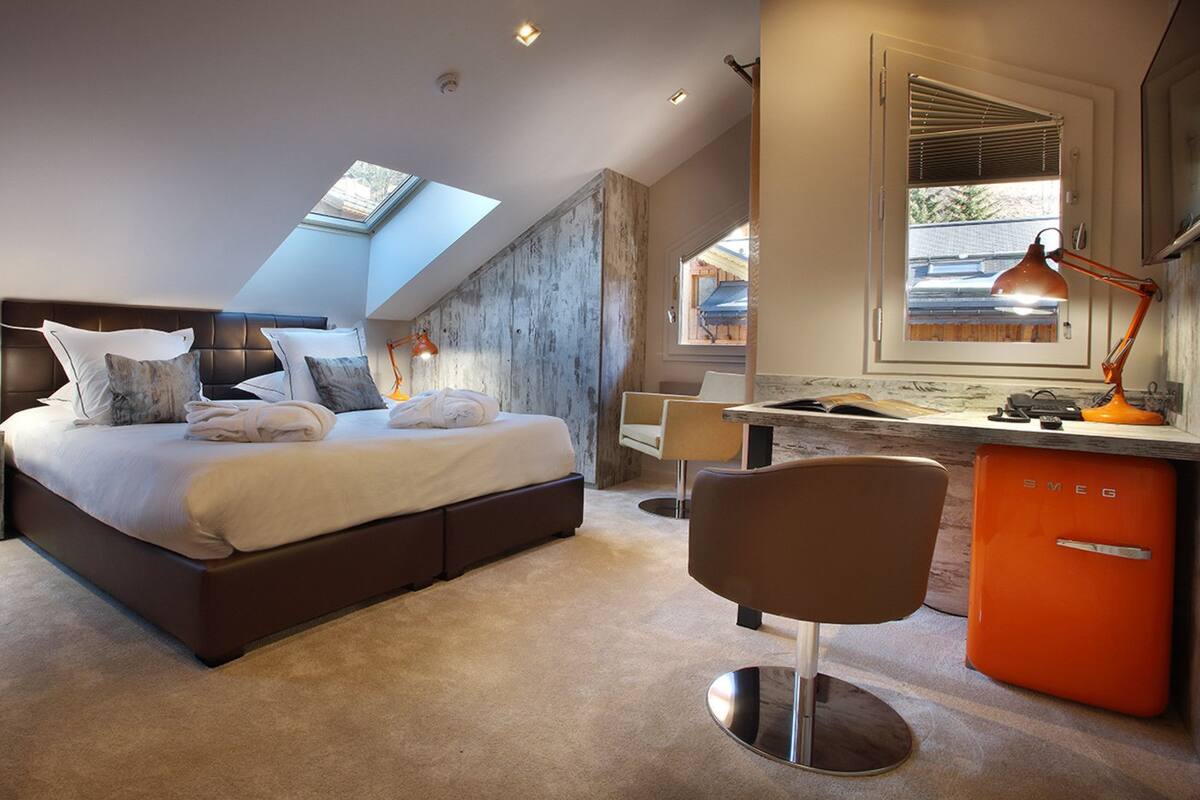 Een moderne slaapkamer met een groot bed, dakraam, bureau met stoel en een kleine keukenhoek.