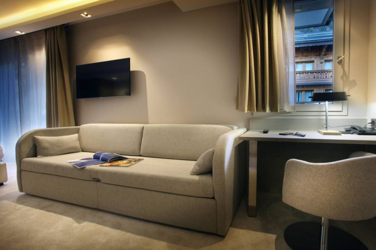 Een moderne hotelkamer met een beige bank, een bureau met een lamp en een televisie aan de muur.
