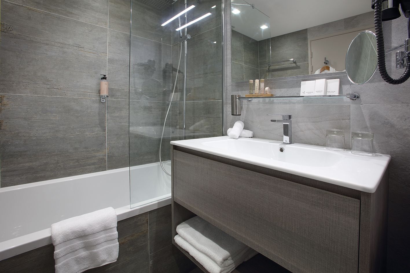 A modern bathroom with a glass-enclosed shower, a white sink with a mirror above it, and a towel rack with towels.