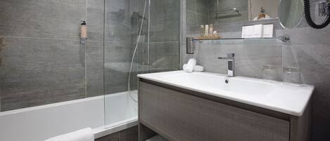 A modern bathroom with a glass-enclosed shower, a white sink with a mirror above it, and a towel rack with towels.
