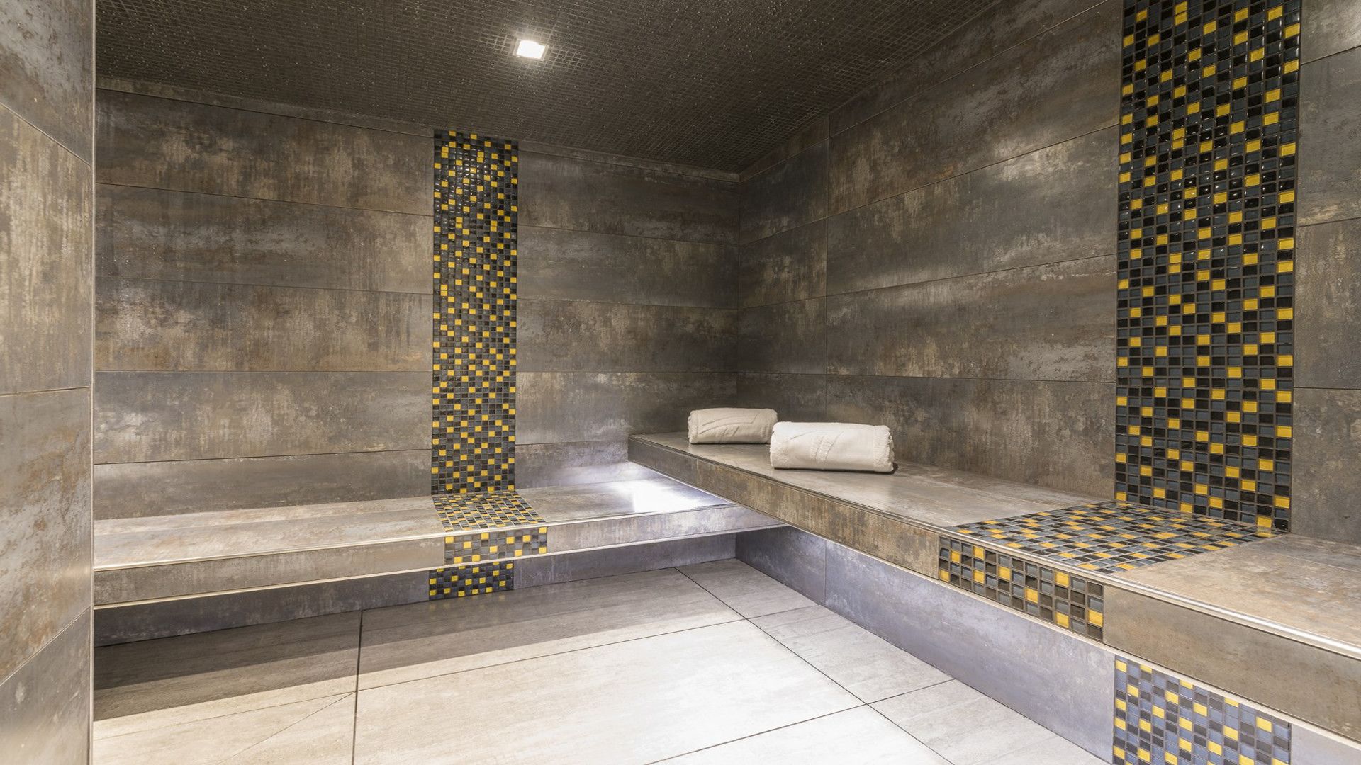 Un baño moderno con una bañera grande, un banco y una pared de azulejos con diseño de cuadros.