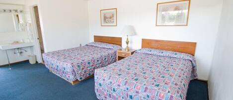 A room with two single beds, a bedside table with a lamp, a mirror, and a small window.