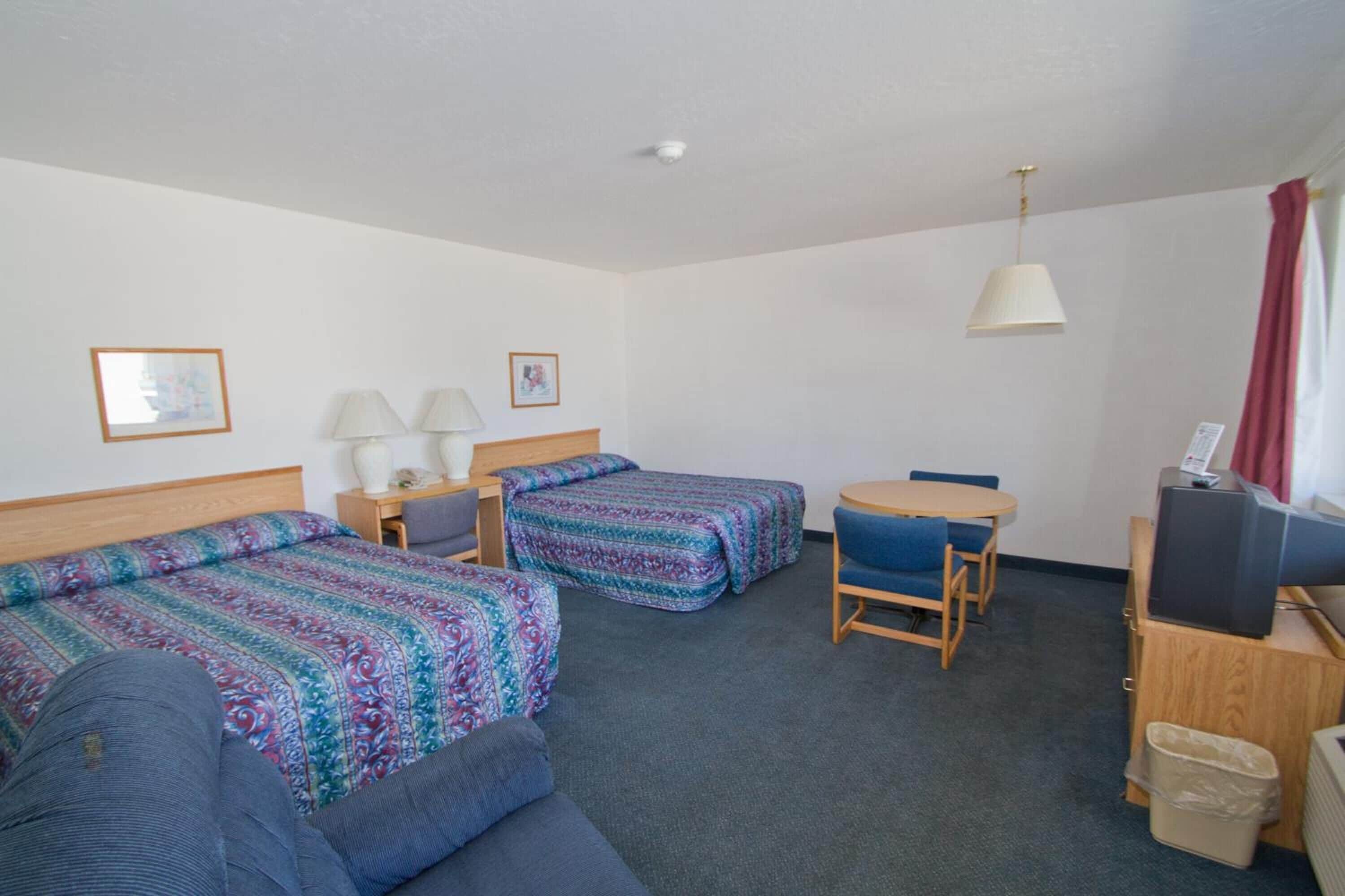 A hotel room with two beds, a desk with a computer, a chair, and a small table.