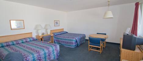 A hotel room with two beds, a desk with a computer, a chair, and a small table.