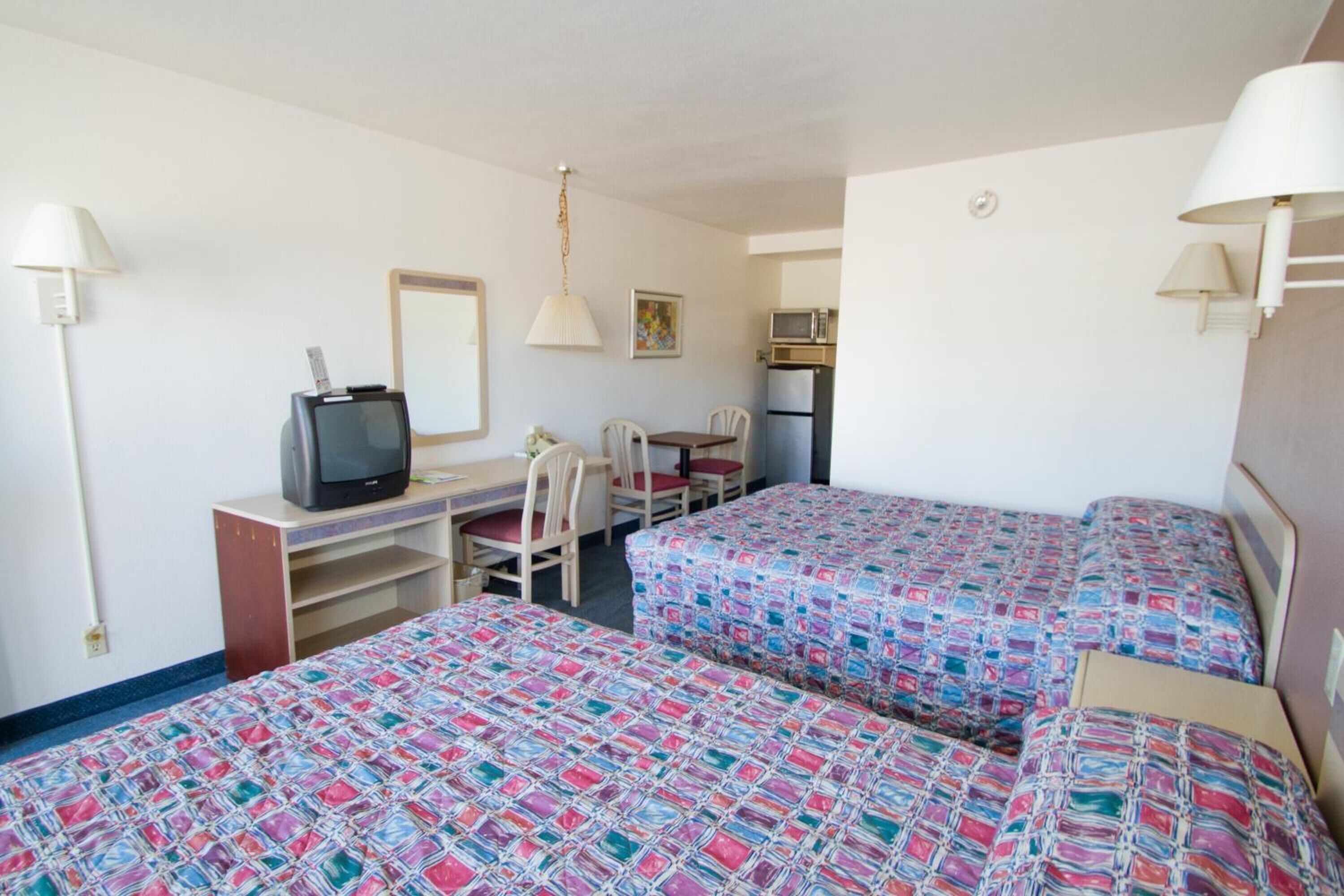 Une chambre d’hôtel avec deux lits, un bureau avec une télévision, une chaise, une table et un four à micro-ondes.