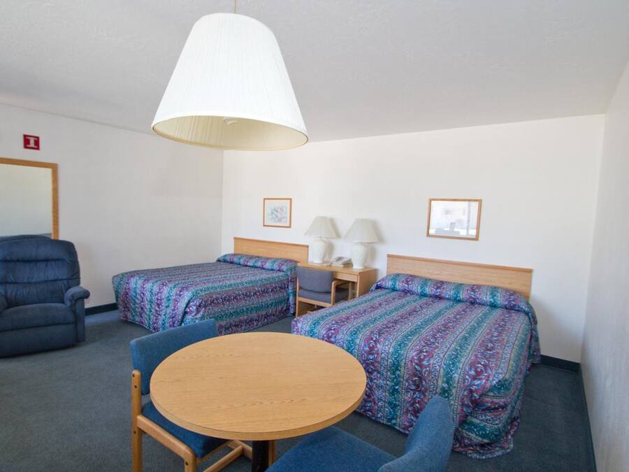 Habitación de hotel con dos camas, una silla, una mesa redonda y una lámpara.