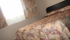 A bedroom with a patterned bedspread, a window with curtains, and a headboard. - Sleep Right Inn (Enderby)