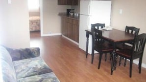 A compact kitchen with wooden cabinets, a white refrigerator, and a dining table with four chairs. - Sleep Right Inn (Enderby)