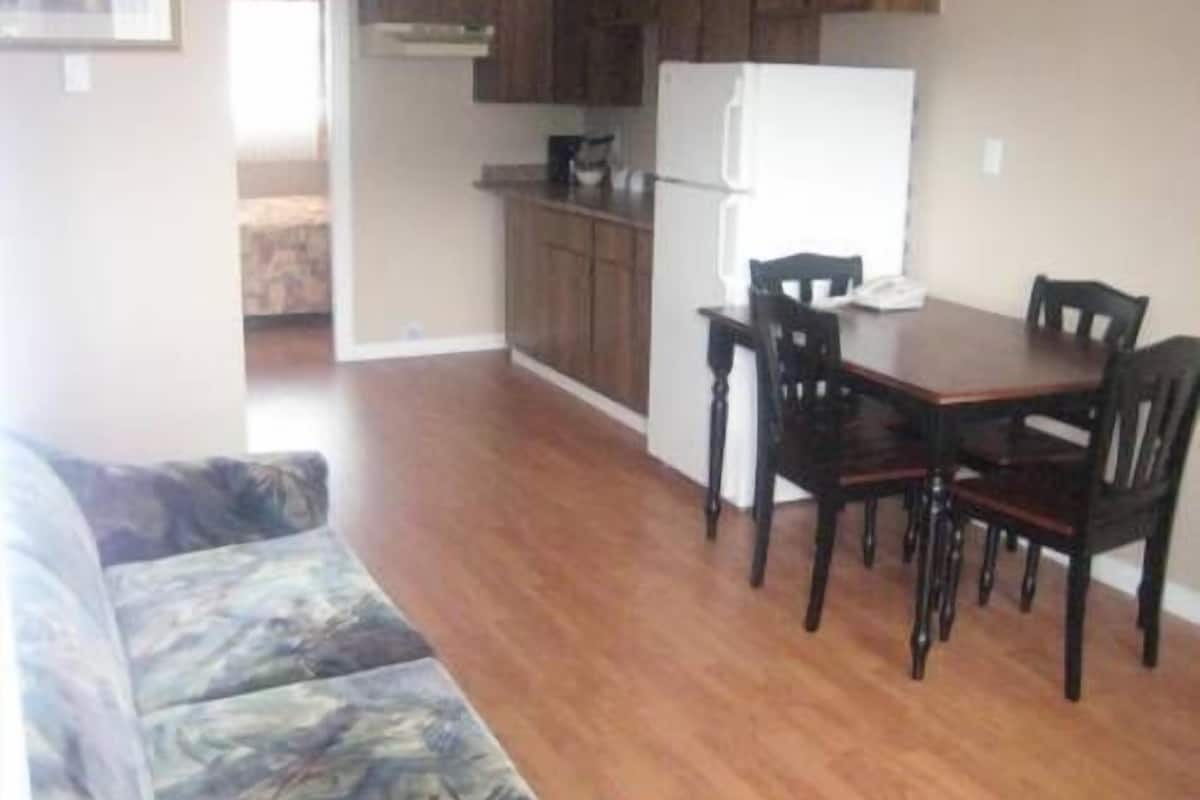 A compact kitchen with wooden cabinets, a white refrigerator, and a dining table with four chairs.