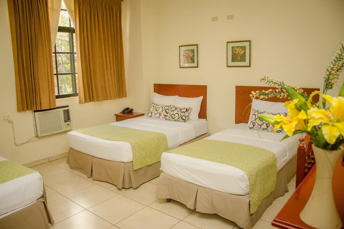 A hotel room with two beds, a window with curtains, a bedside table with a phone, and a vase with flowers.