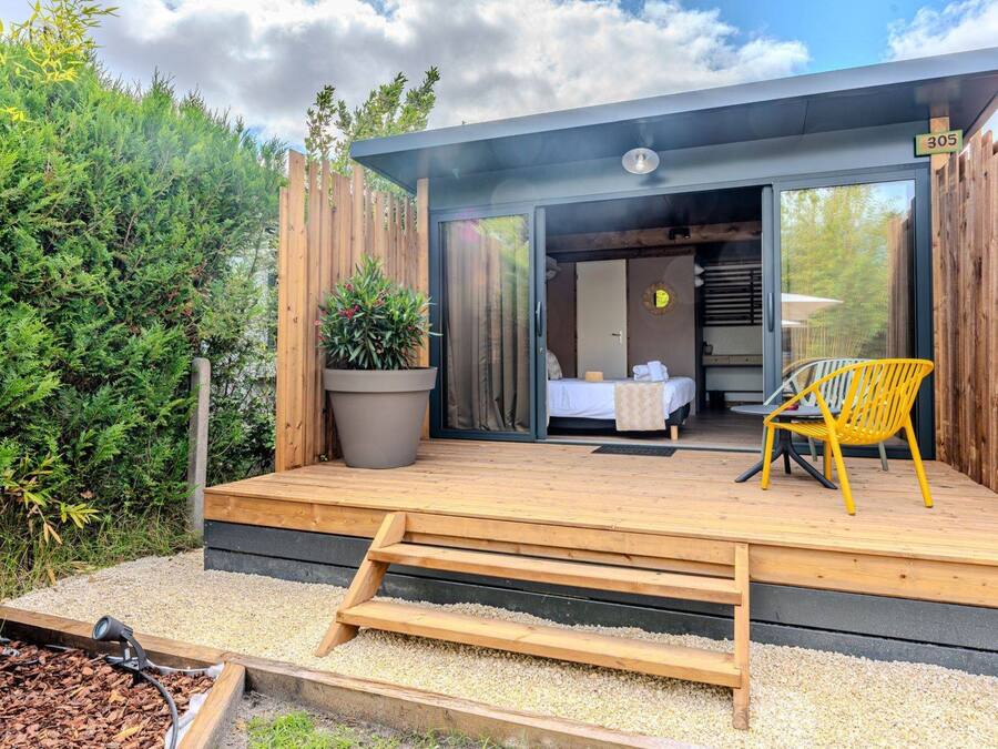 A modern outdoor room with a bed, a chair, and a large potted plant.