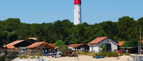 A coastal village with a prominent lighthouse, small boats, and traditional houses with red roofs.